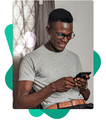 Homem sorridente, com óculos, sentado e usando celular. Ele calcula a sua margem consignável de forma simples e rápida no site da Konsi.